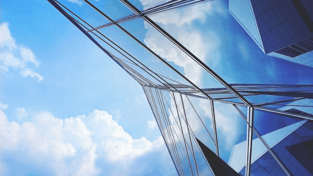 Fachada de prédio moderno com vidros espelhados refletindo o céu azul e nuvens.