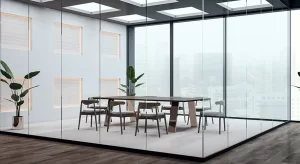 Sala de reunião moderna com paredes de vidro, mesa retangular de madeira, cadeiras minimalistas e plantas decorativas, com vista para prédios ao fundo através de grandes janelas.