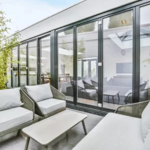 Esquadrias de Alumínio em portas de vidro de correr com perfis escuros, integrando área externa com ambiente interno moderno, proporcionando ampla entrada de luz natural e visual sofisticado.